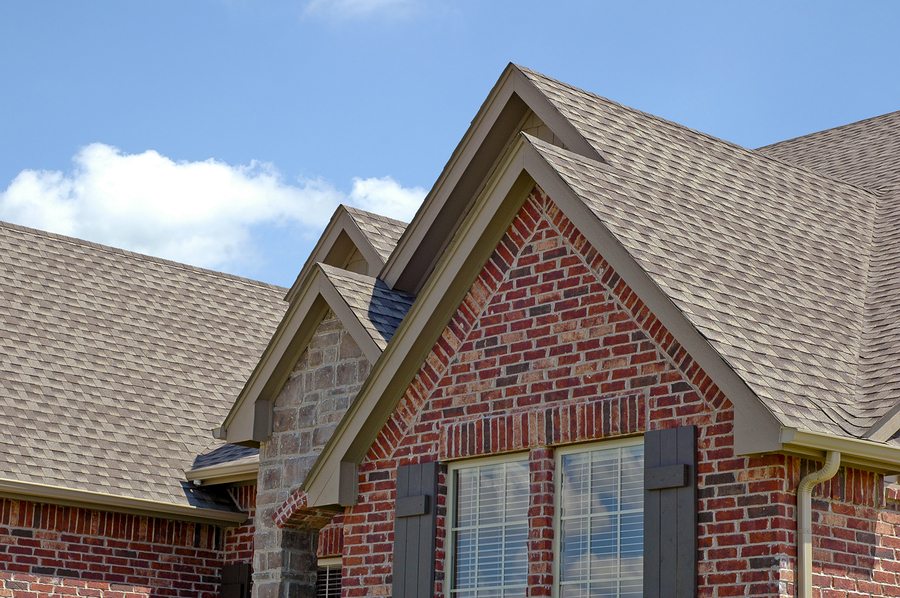 Brick home with newly installed brown/gray roof. Blue sky in background.