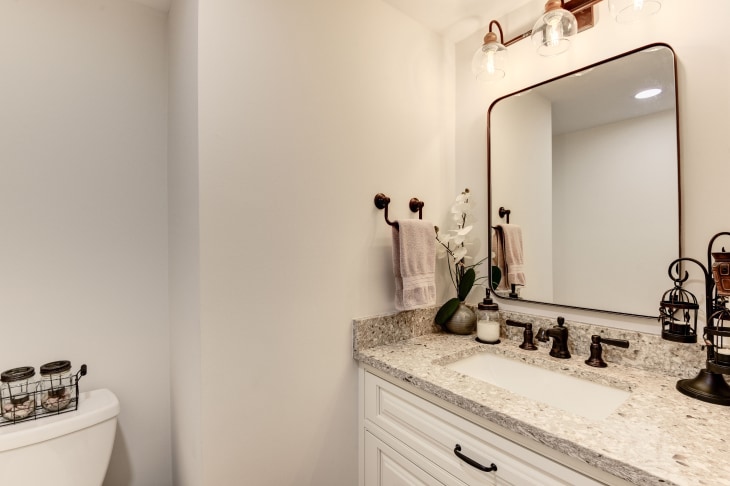 Bathroom remodel with white vanity, granite countertop, modern mirror and light fixtures, white walls.