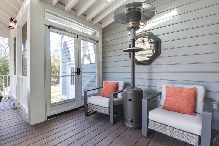 Covered deck with cushioned patio chairs. Light gray siding of home exterior behind chairs. Chairs have pop of peachy color in throw pillows on each.