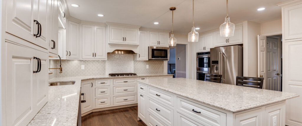 Remodeled kitchen with white cabinets, white stone countertops, wood floors, recessed and pendant lighting.